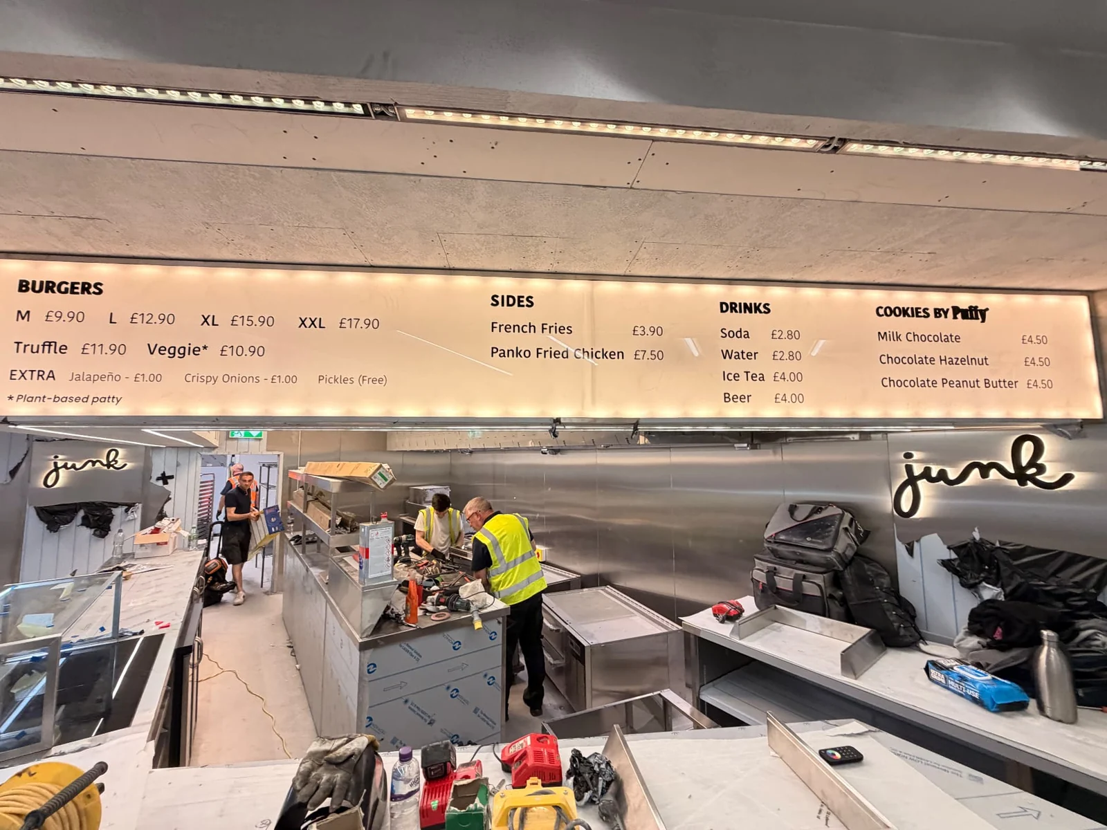 Illuminated Junk menu board above a stainless steel counter, with halo-lit wall lettering behind