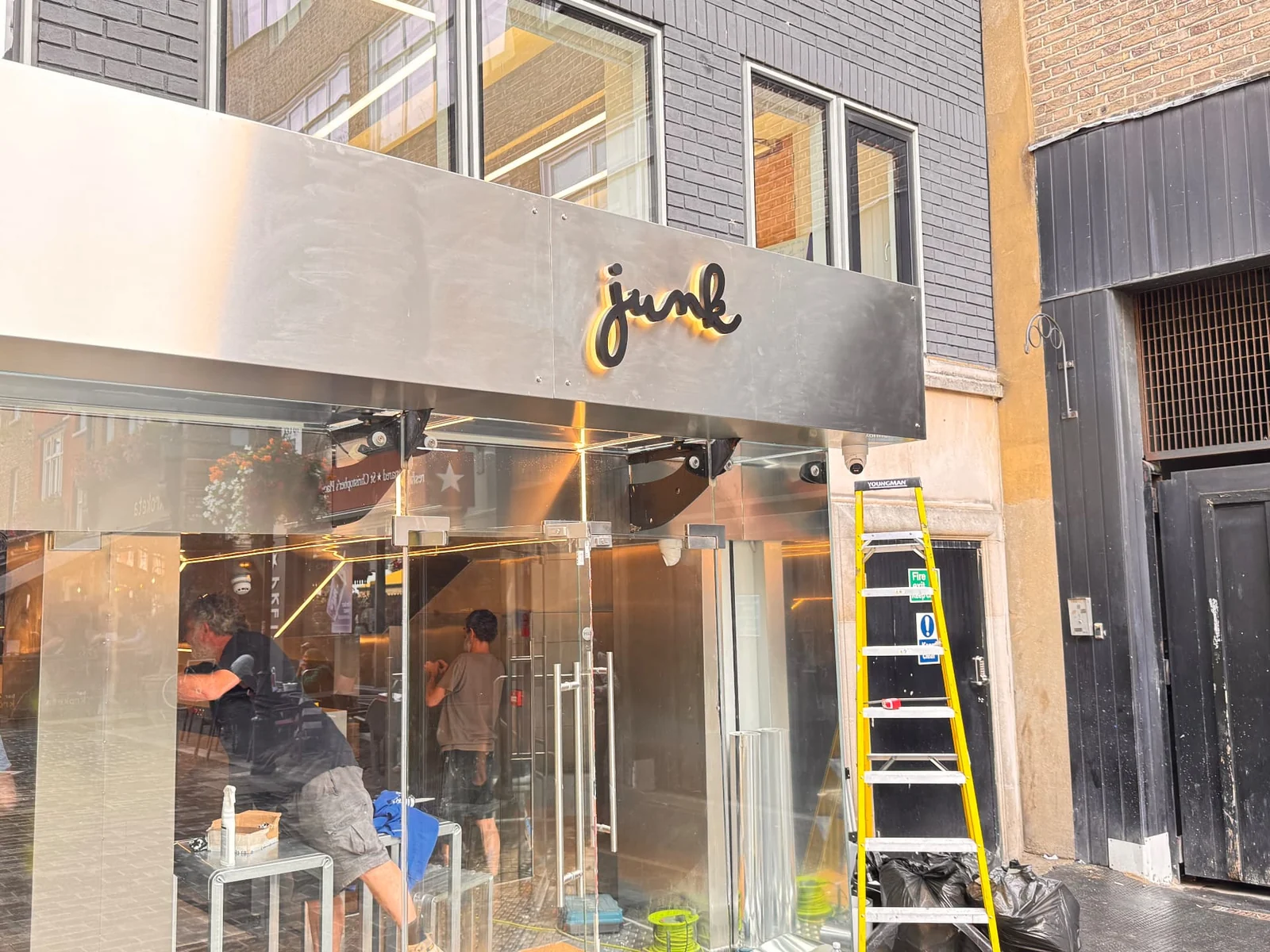 Angled view of a brushed stainless steel Junk fascia with halo-lit lettering above glazed entrance doors