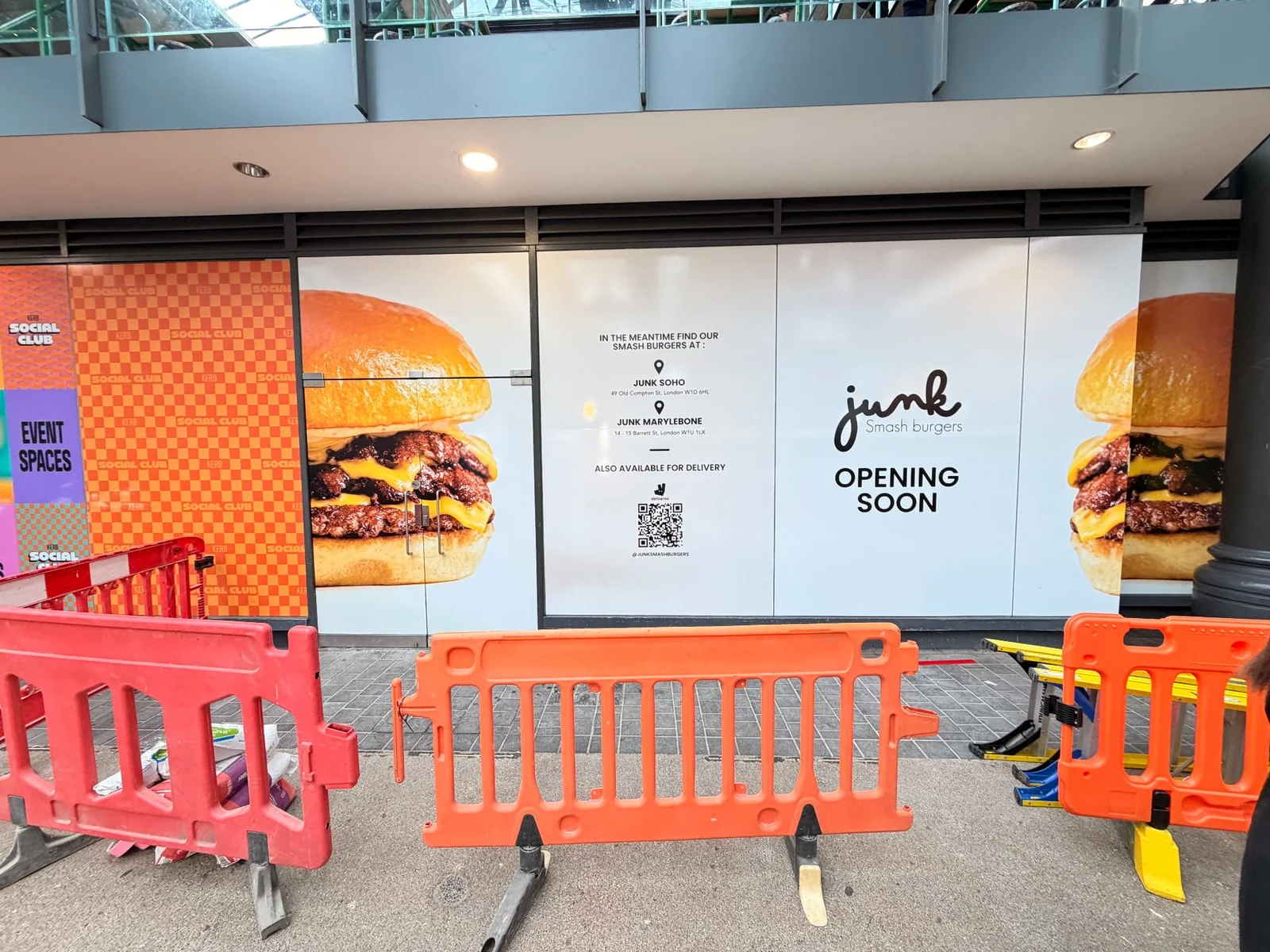 Junk printed hoarding panels in a covered market concourse, fronted by pedestrian barriers