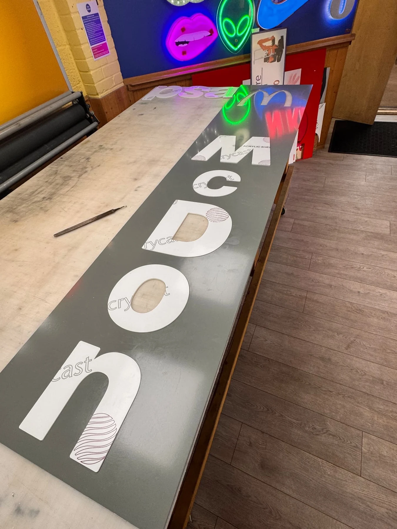 White acrylic lettering being fitted into routed aluminium panels on the workshop bench
