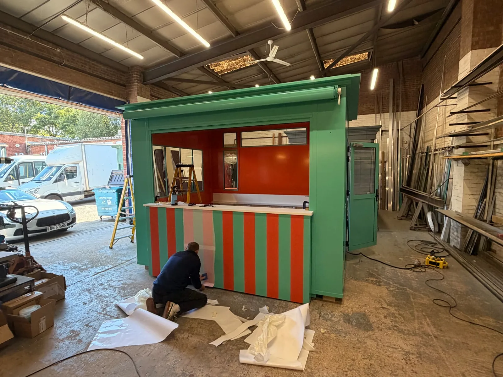 Installer kneeling to apply striped vinyl to the counter of the kiosk inside the manufacturer’s workshop