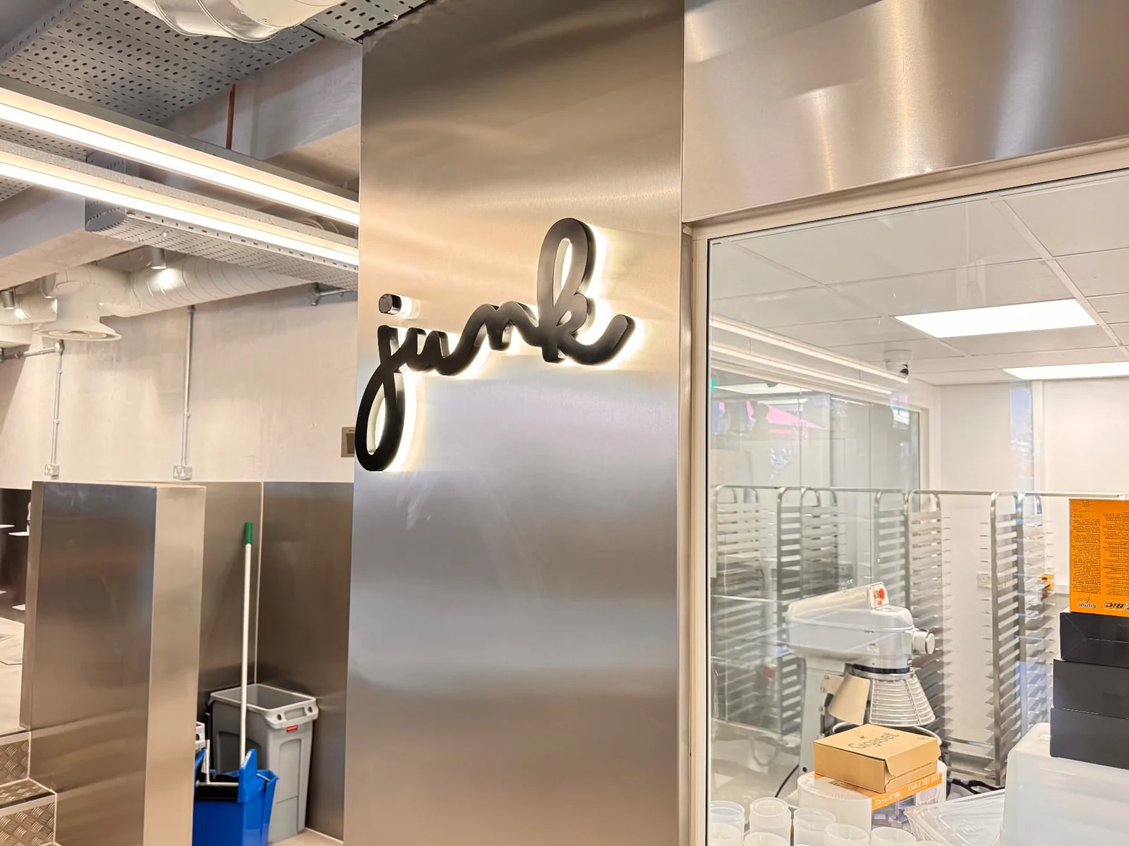 Halo-lit Junk lettering on a stainless steel column beside a glazed kitchen viewing window