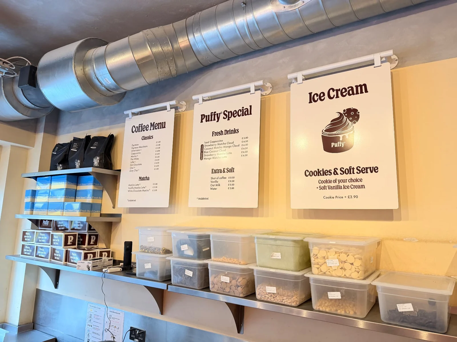 Puffy menu boards mounted on white tubular wall brackets above a stainless steel prep counter