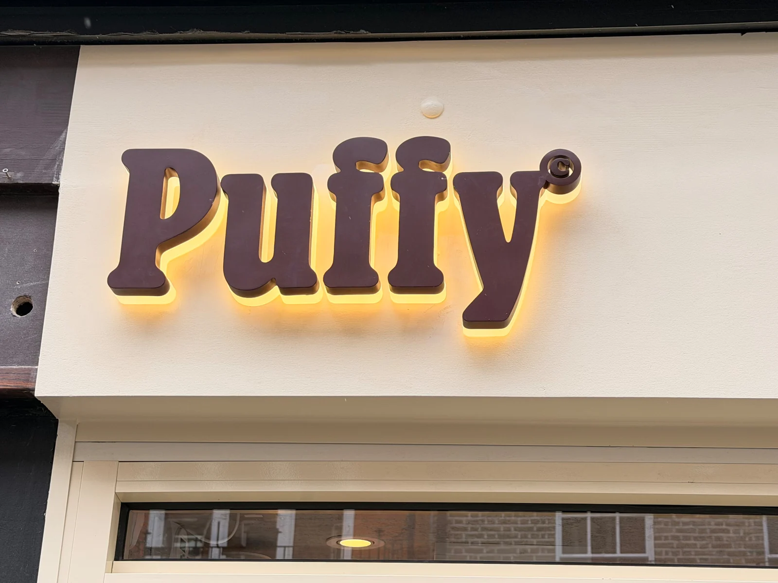 Halo-lit Puffy 3D letters glowing against a cream fascia