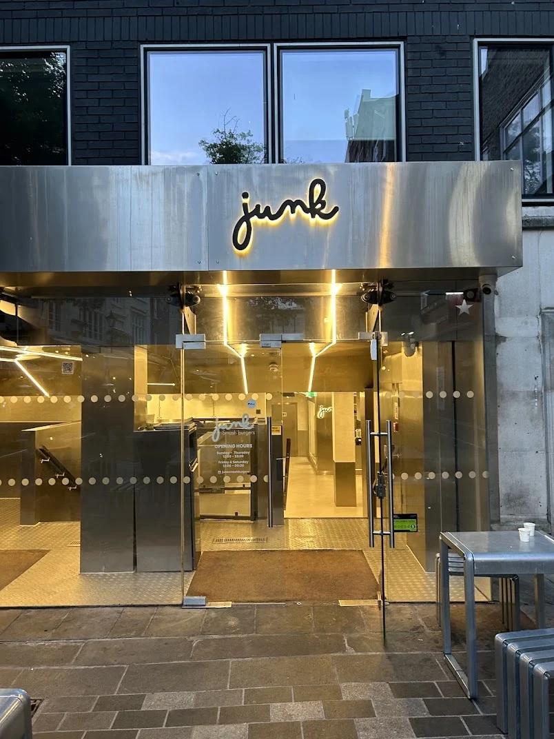 Junk glazed entrance doors with frosted manifestation dots, opening-hours vinyl and halo-lit fascia lettering above