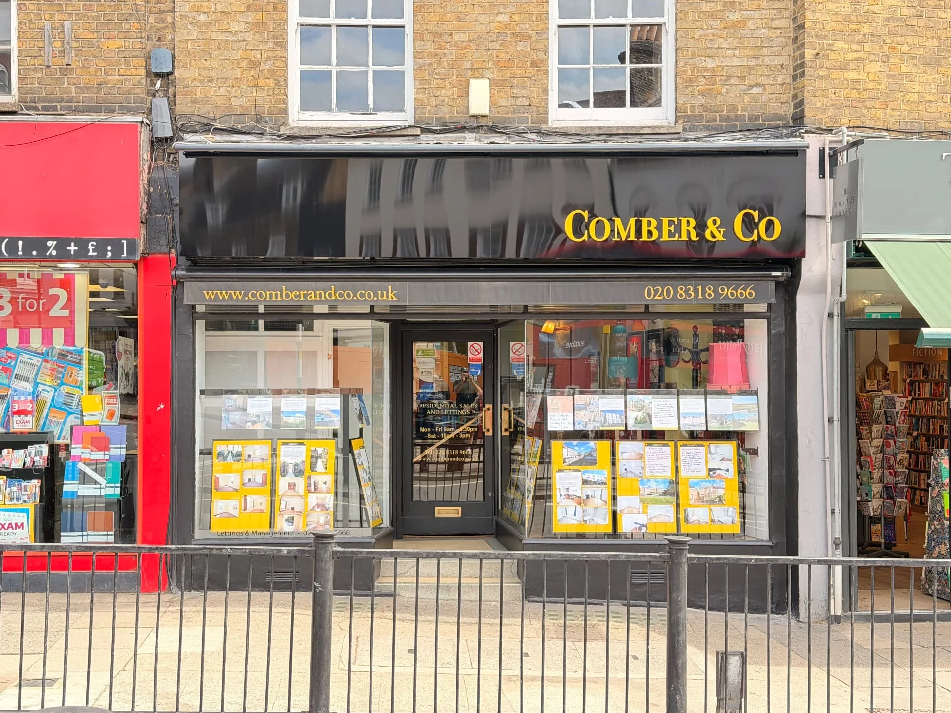 Completed Comber & Co shopfront in Blackheath, viewed straight on, with restored stainless steel lettering on a gloss-black sign tray and an external LED trough light above