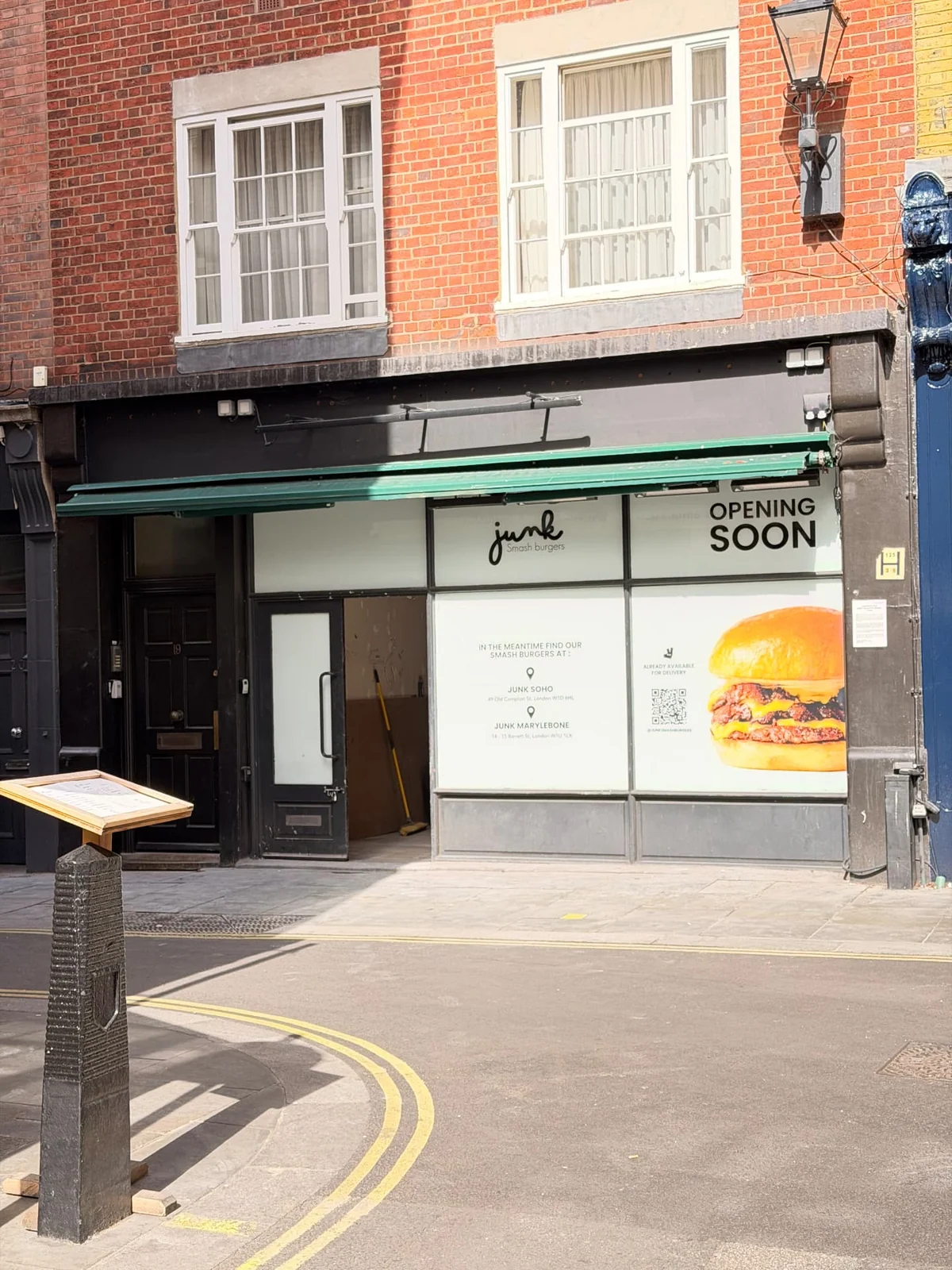 Junk printed window wrap with opening-soon graphics and a wooden menu lectern on the pavement