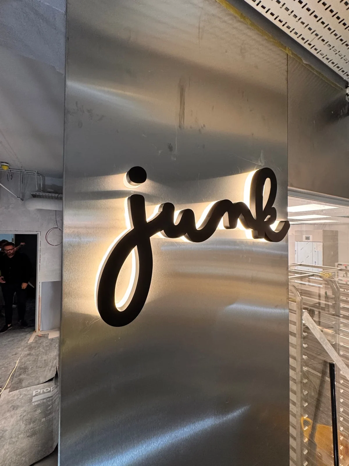 Brushed stainless steel interior column carrying black halo-lit Junk script lettering