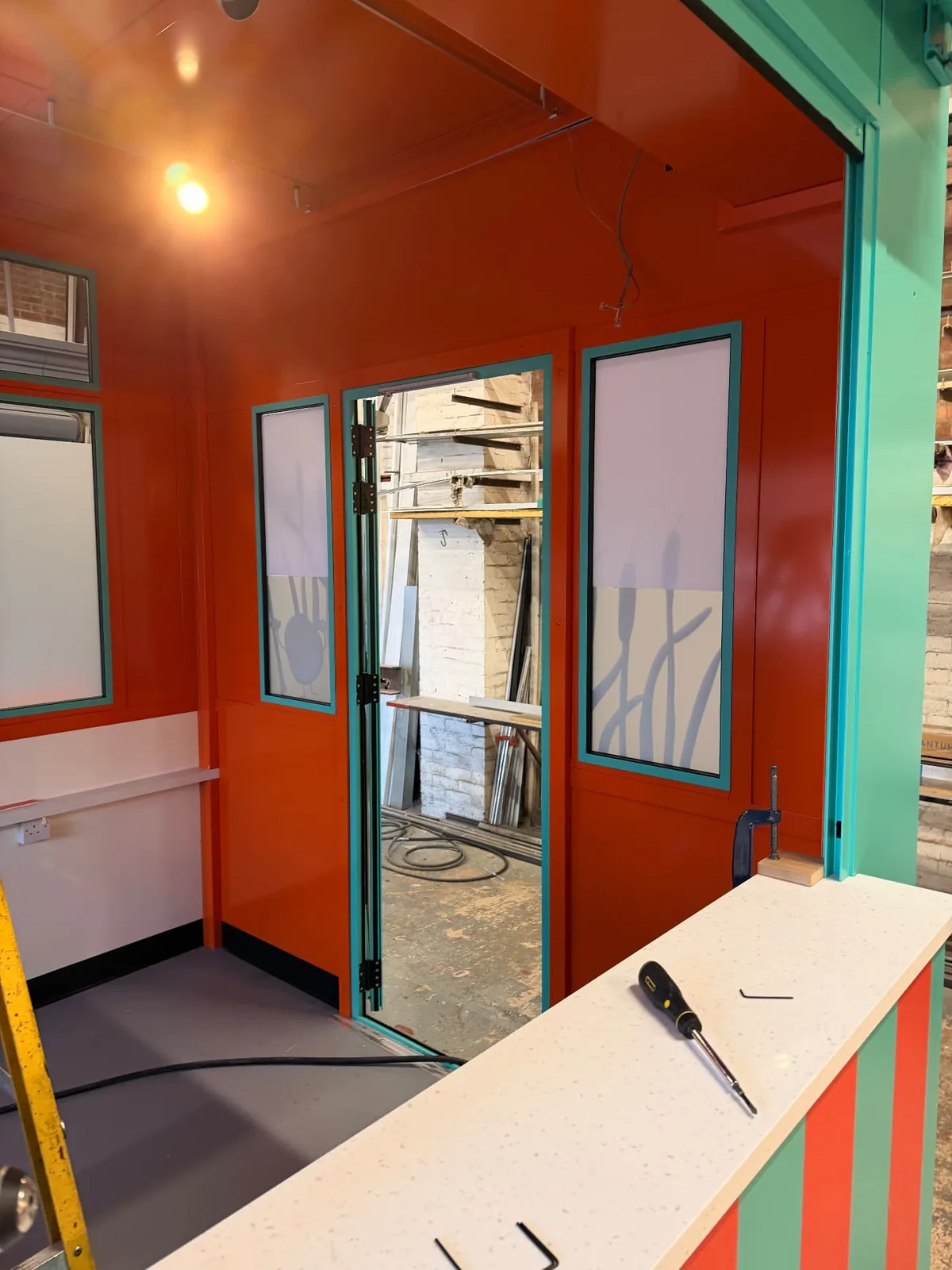 Orange kiosk interior with bulrush window coverings on the glazed panels, during fit-out at the manufacturer’s premises