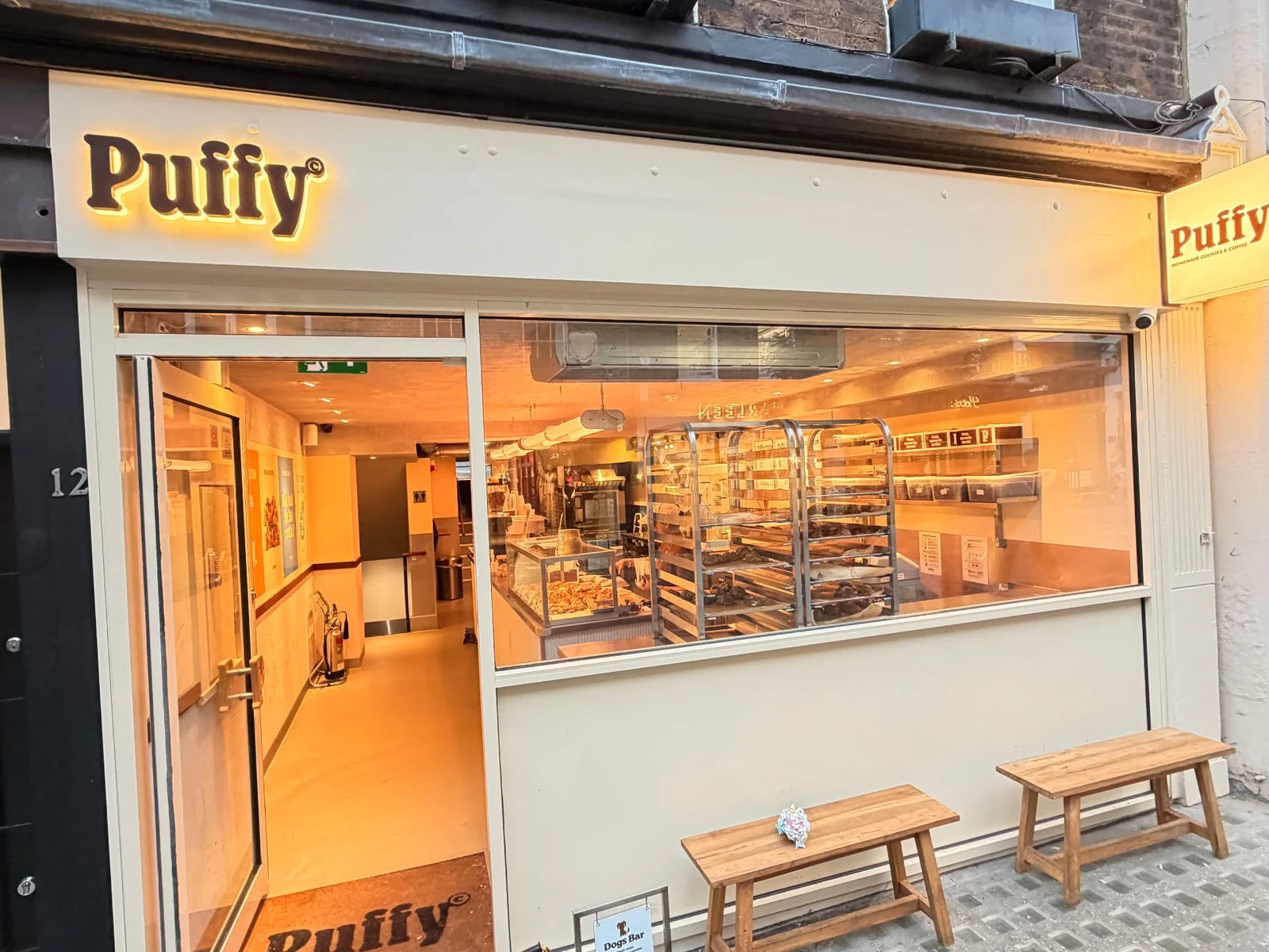 Puffy shopfront with halo-lit fascia letters, an illuminated projecting sign, branded entrance mat and window graphics