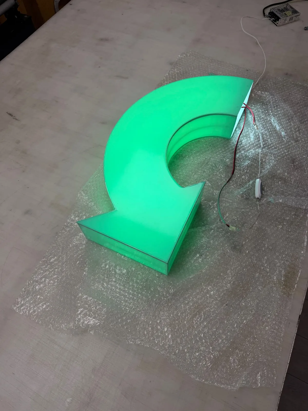 Curved acrylic arrow glowing green during a workshop lighting test, before the Crumpets lettering was applied
