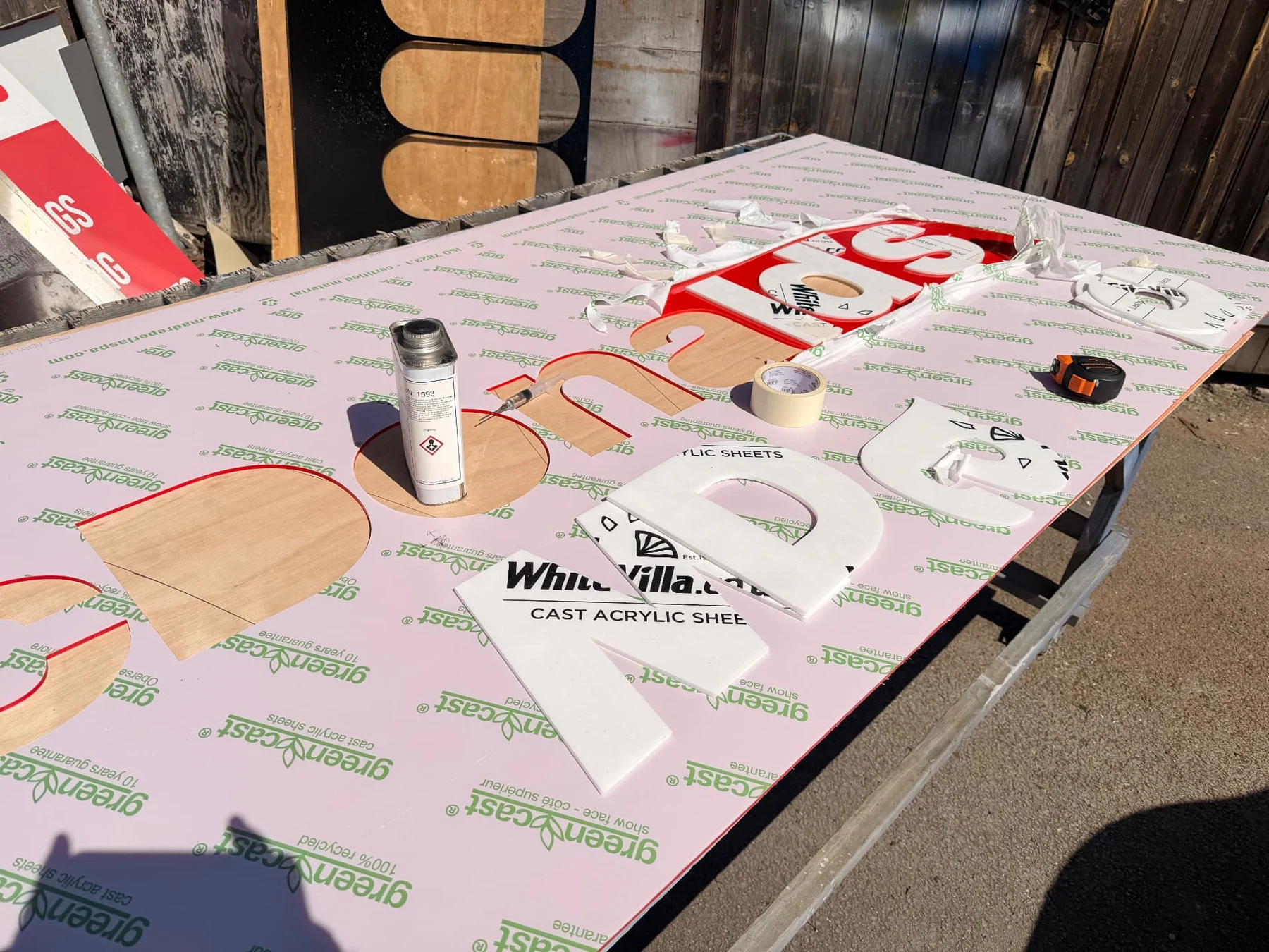 Separate white acrylic letters being fitted into an oversized red totem sign face with protective masking