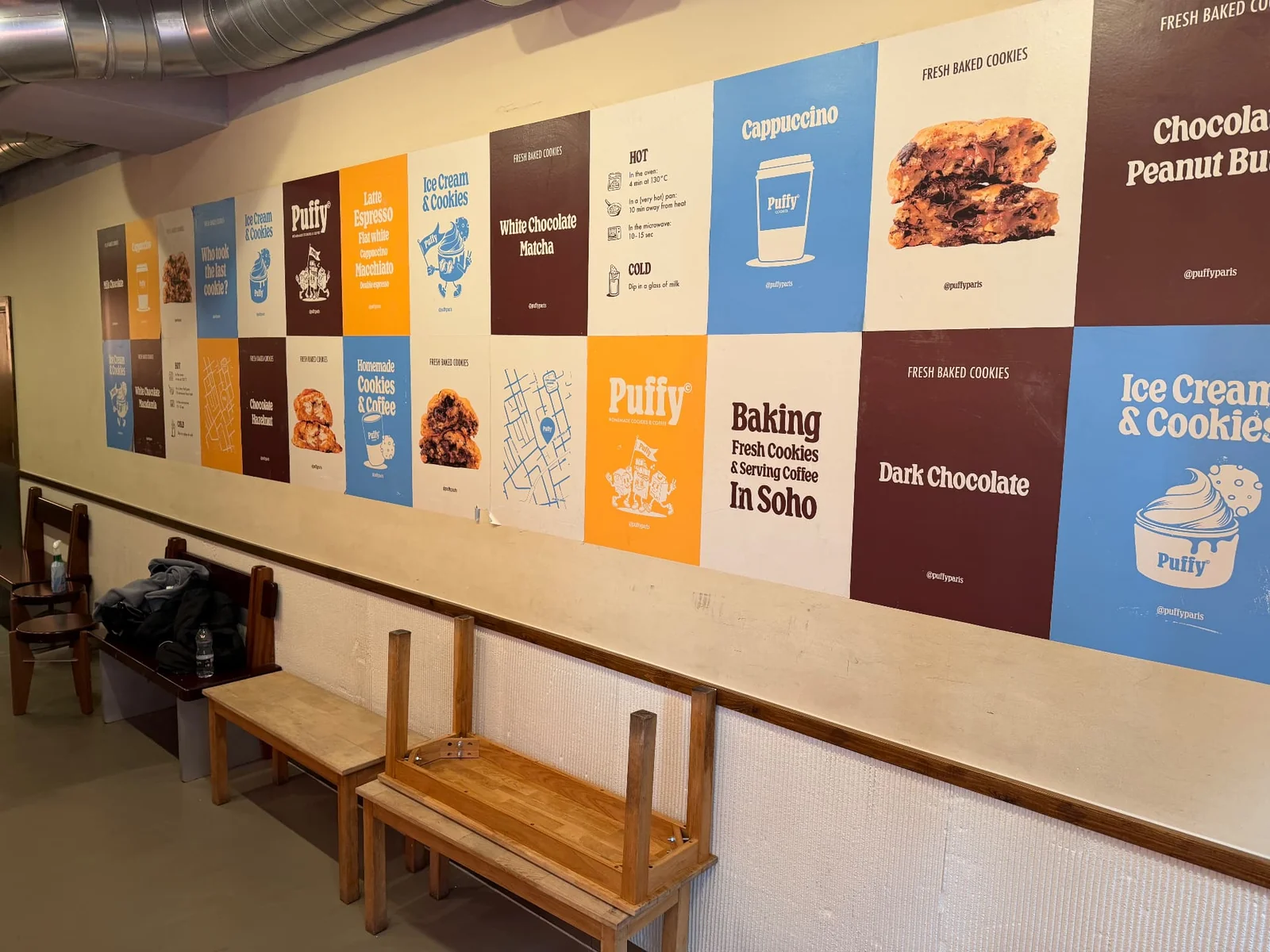 Tiled wall of Puffy printed posters above a bench, including a panel reading “In Soho”